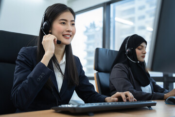 Two women in business attire are working at a desk with a keyboard and a headset. One woman is talking on the phone. the other woman is typing. They work as operators in the office.