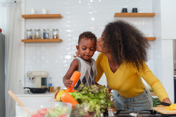 Happy African mother and son making salad while preparing food in the kitchen having fun, mother and son cooking activity concept.