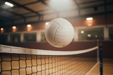 A white volleyball suspended in mid air above a net in a dimly lit indoor gymnasium with spotlights illuminating the ball