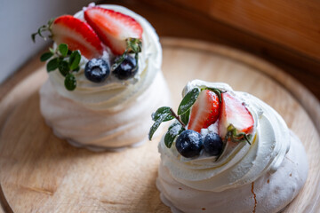 Pavlova dessert featuring delicate meringue topped with fresh strawberries and blueberries,...
