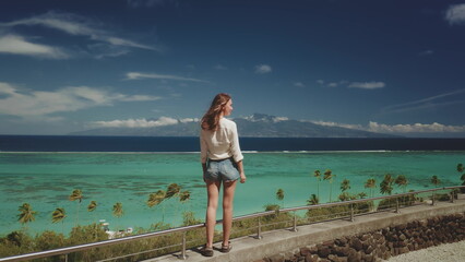 Young tourist enjoys the stunning panoramic view of moorea island's turquoise lagoon and lush green mountains from a scenic lookout point, capturing the essence of a perfect tropical getaway