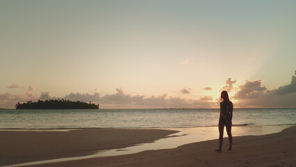 Young woman walking sunset sandy beach. Silhouette of slim girl against colorful sky and calm ocean. Female in bikini relax and enjoy summer holiday vacation on tropical island. Bright orange sky