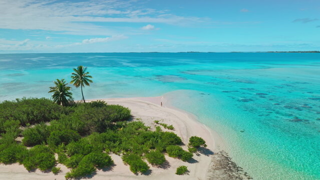 Aerial drone view of a woman walking on a pristine white sand beach, surrounded by turquoise water and lush green vegetation. The perfect destination for a relaxing and unforgettable vacation