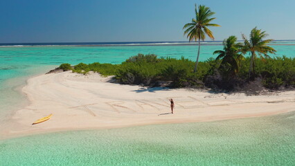 Woman walking on a white sand beach near turquoise sea water and travel writing, enjoying summer vacation in a tropical paradise with palm trees and kayak