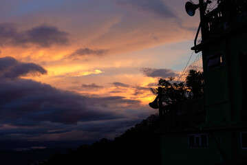 Fiery sunset clouds glowing over dark mountain silhouettes and a house balcony with planys in the foreground