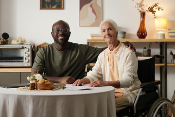 Portrait of Black man sitting beside senior Caucasian woman with disability in wheelchair, both...