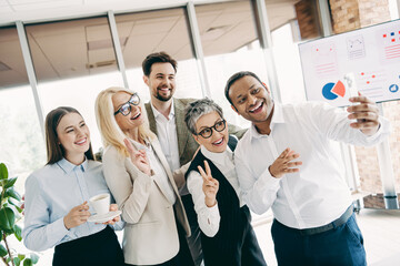 Cheerful coworkers taking a selfie during a meeting in a modern office environment, representing teamwork and diversity