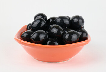 Bowl filled with glossy black olives on a white surface