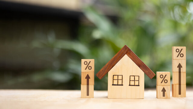 Wooden house with percentage blocks and upward arrows symbolizing rising mortgage rates and housing finance