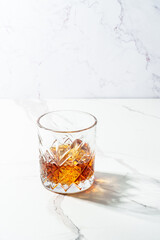 Whiskey with ice cube in the glass at white table.