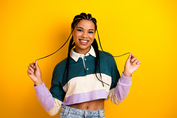Portrait of a cheerful young woman posing in a striped crop top with braids on yellow background