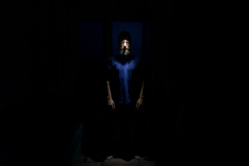 Bearded man standing in complete darkness with face illuminated by headlamp. Dramatic portrait with mysterious atmosphere, symbolizing night exploration, survival, and adventure