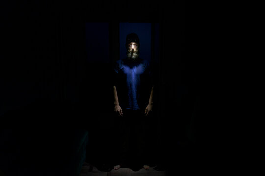 Bearded man standing in complete darkness with face illuminated by headlamp. Dramatic portrait with mysterious atmosphere, symbolizing night exploration, survival, and adventure - Powered by Adobe