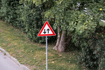 Traffic sign indicating one-way street direction near a green park area in the afternoon