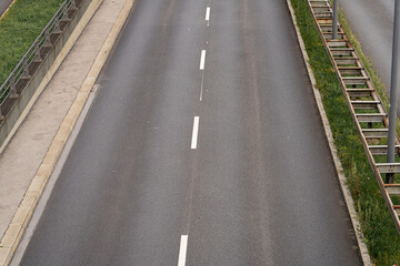 Empty road stretches under a cloudy sky with green grass on one side and railings on the other