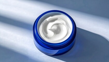 A glossy, cobalt blue jar of luxurious, creamy lotion sits atop a light blue surface, catching the light.