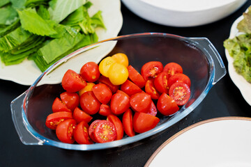 Freshly halved cherry tomatoes in a glass bowl, ready for a salad, with leafy greens in the...