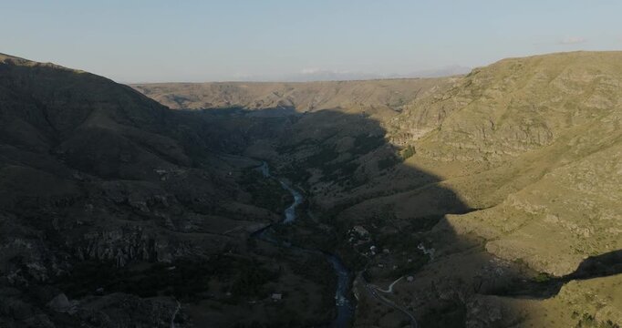Aerial view of a sinuous river carving its path through a dramatic valley, the landscape painted in contrasting light and shadow, Gogasheni, Samtskhe-Javakheti, Georgia.
