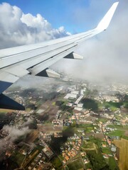 Airplane wing above lush green fields and urban areas, capturing the beauty of nature and cityscape...