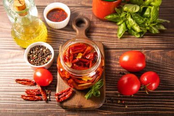 Dried organic tomatoes preservation with herbs and olive oil in jar.