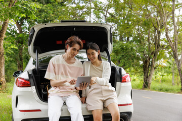 Happy young Asian couple enjoy check out the map from a tablet in the car while travel in the tropical forest