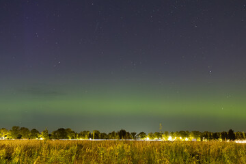 A faint green aurora glows above the horizon, blending with the starry night sky over a quiet field...