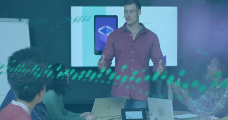 Presenting man in maroon shirt gesturing toward display in conference room, with laptops and tablet