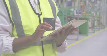 Using tablet smartphone, technician wearing safety vest inspecting factory floor, copy space © vectorfusionart