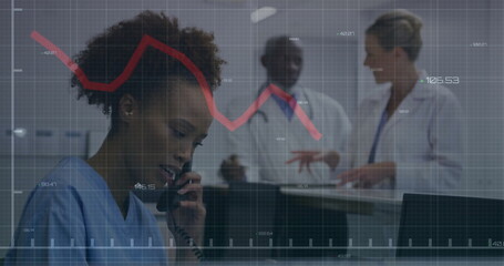 Answering nurse in blue scrubs handling telephone at hospital desk, with data graph, copy space