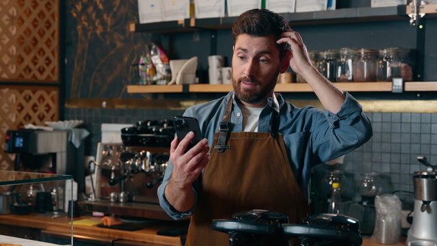 Confused Caucasian barista employee guy waiter owner worker male man using mobile phone upset manager owner entrepreneur demonstrating gadget green screen smartphone in cafeteria frustration tech app - Powered by Adobe