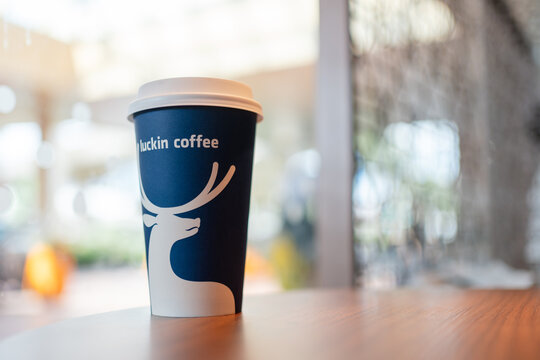 KUALA LUMPUR, MALAYSIA - AUG 17, 2025: Luckin Coffee blue takeaway cup with white deer logo and branding placed on a wooden caf&eacute; table in a brightly lit indoor setting.