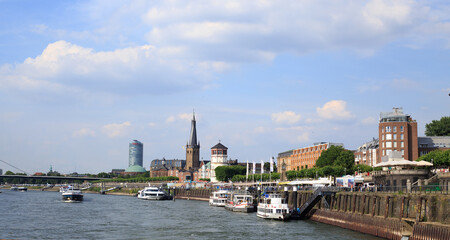 Fototapeta premium Dusseldorf , Germany. Busy port where tour boats and river cruise boats dock to allow passengers off to explore the City. St Lambertus Church is in the background