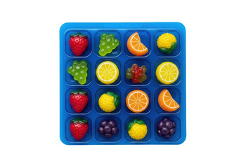 Translucent deep blue blister pack with distinct compartments, holding vibrant fruit-shaped gummy candies on a transparent background, top-down studio shot, sweet indulgence concept