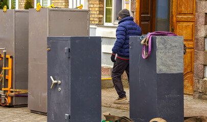 Worker transporting heavy safes outside a building during daylight hours in an urban area