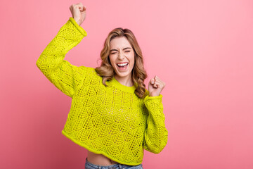 Adorable young woman in bright yellow knitwear smiling cheerfully against a vibrant pink background...