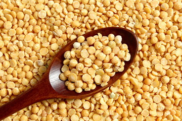 A wooden spoon with dry yellow peas lies on the surface.	