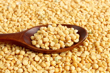 A wooden spoon with dry yellow peas lies on the surface.	