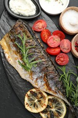 Tasty roasted mackerel served with spices and sauce on black table, flat lay. Homemade seafood dish