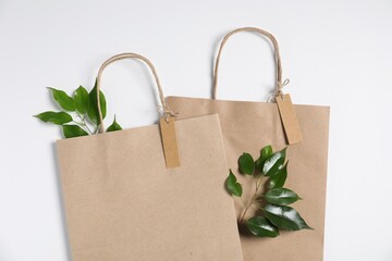 Eco friendly packaging. Paper bags and leaves on white background, flat lay