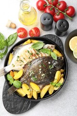 Tasty roasted flounder fish with herbs, potato, lemon slices and tomatoes on light table, flat lay. Homemade seafood dish