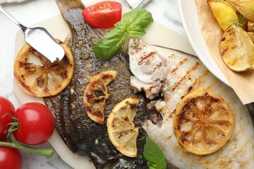 Tasty roasted flounder fish served with potatoes, tomatoes, basil and lemon slices on white marble table, flat lay. Homemade seafood dish
