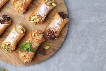 Delicious cannoli with cheese, nuts, powdered sugar, chocolate and mint on grey table, top view. Space for text
