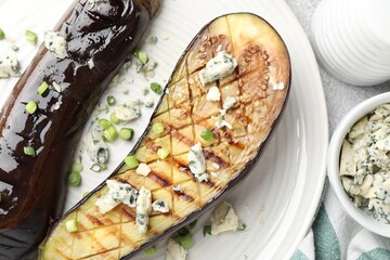Slices of grilled eggplant with green onion and blue cheese on white table, flat lay