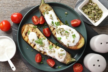 Slices of grilled eggplant with pumpkin seeds, tomatoes and yoghurt on wooden table, flat lay