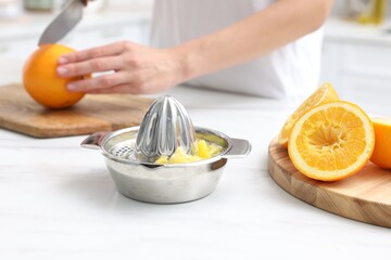 Making juice. Woman cutting orange at white marble table indoors, focus on juicer and fruits