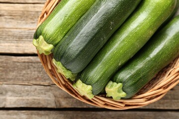Fresh ripe zucchinis in wicker basket on wooden table, top view