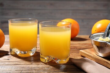 Freshly squeezed orange juice, fruits and juicer on wooden table, closeup