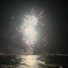 A stunning display of bright white fireworks exploding in the night sky over a body of water. The...