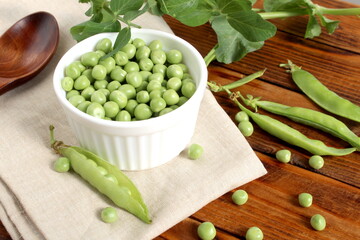 There is a wooden cup with green fresh peas on the wooden table.	