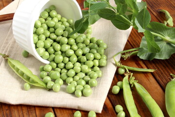 There is a wooden cup with green fresh peas on the wooden table.	